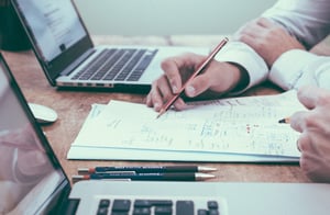 Writing on documents beside laptop